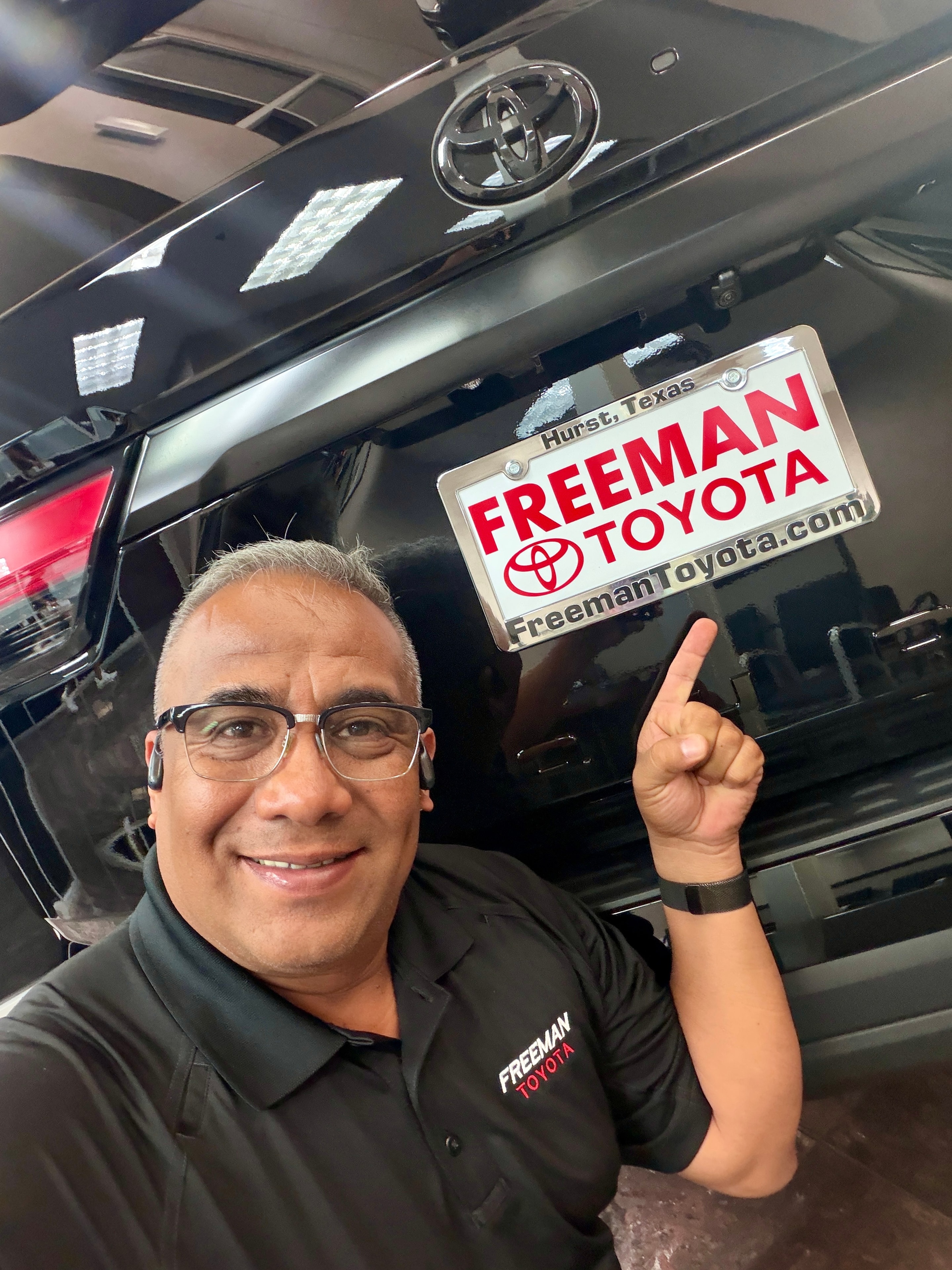 Jesus Esparza pointing at Freeman Toyota license plate frame in Hurst TX